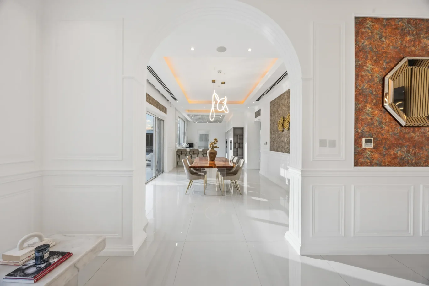 Bright, open dining area seen through an arched doorway with a wooden table and beige chairs under a modern chandelier.