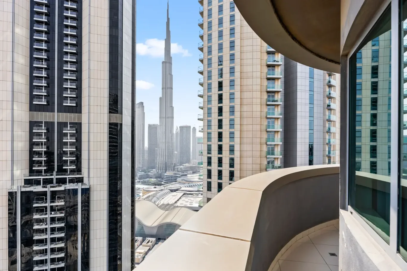 Balcony view from a high-rise apartment overlooking a dense cluster of modern skyscrapers on a sunny day.