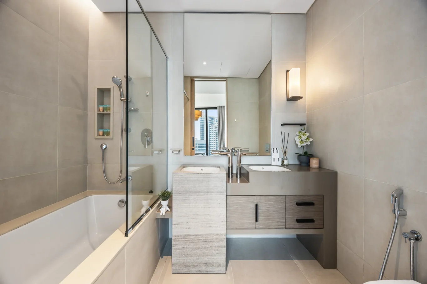 Modern bathroom with a glass-enclosed shower, built-in tub, and gray tiled walls; a double-sink vanity reflects in the mirror.