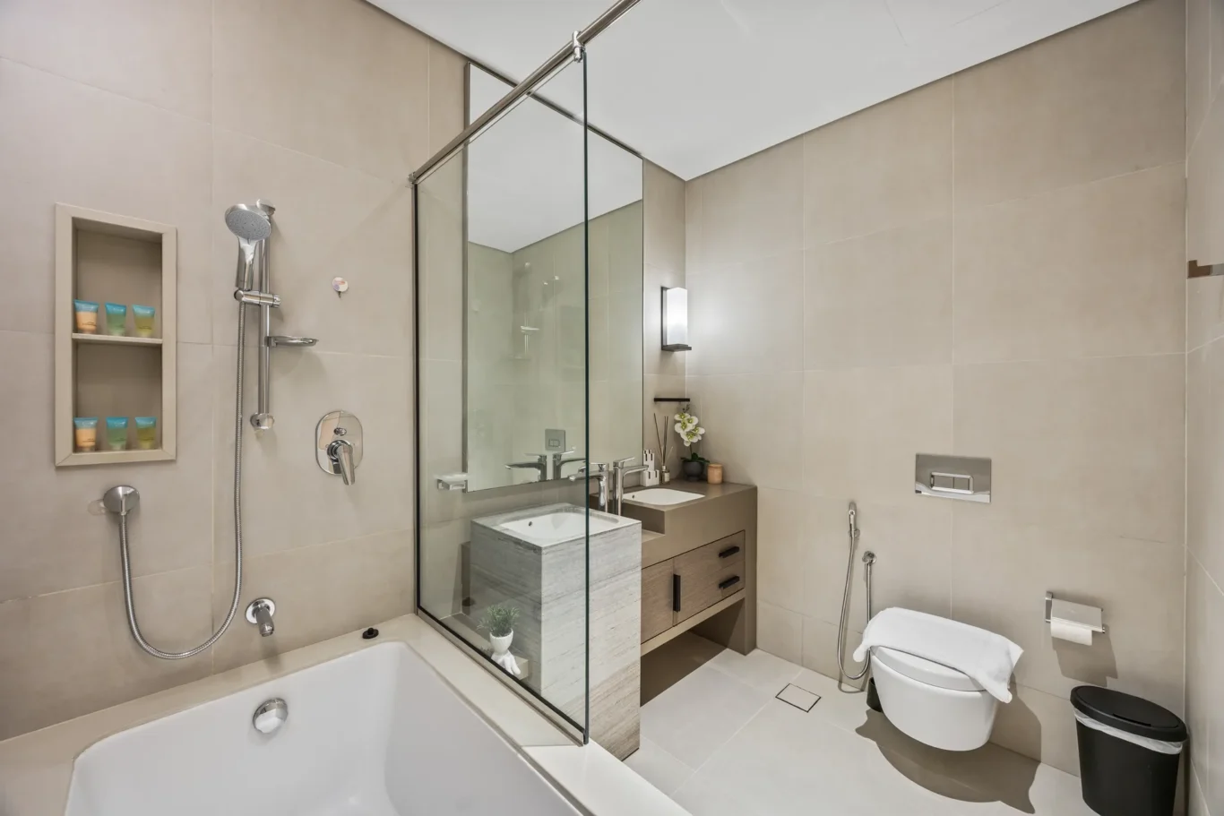 Modern bathroom featuring a glass shower enclosure, bathtub, vanity with sink, and wall-mounted toilet with towel nearby.