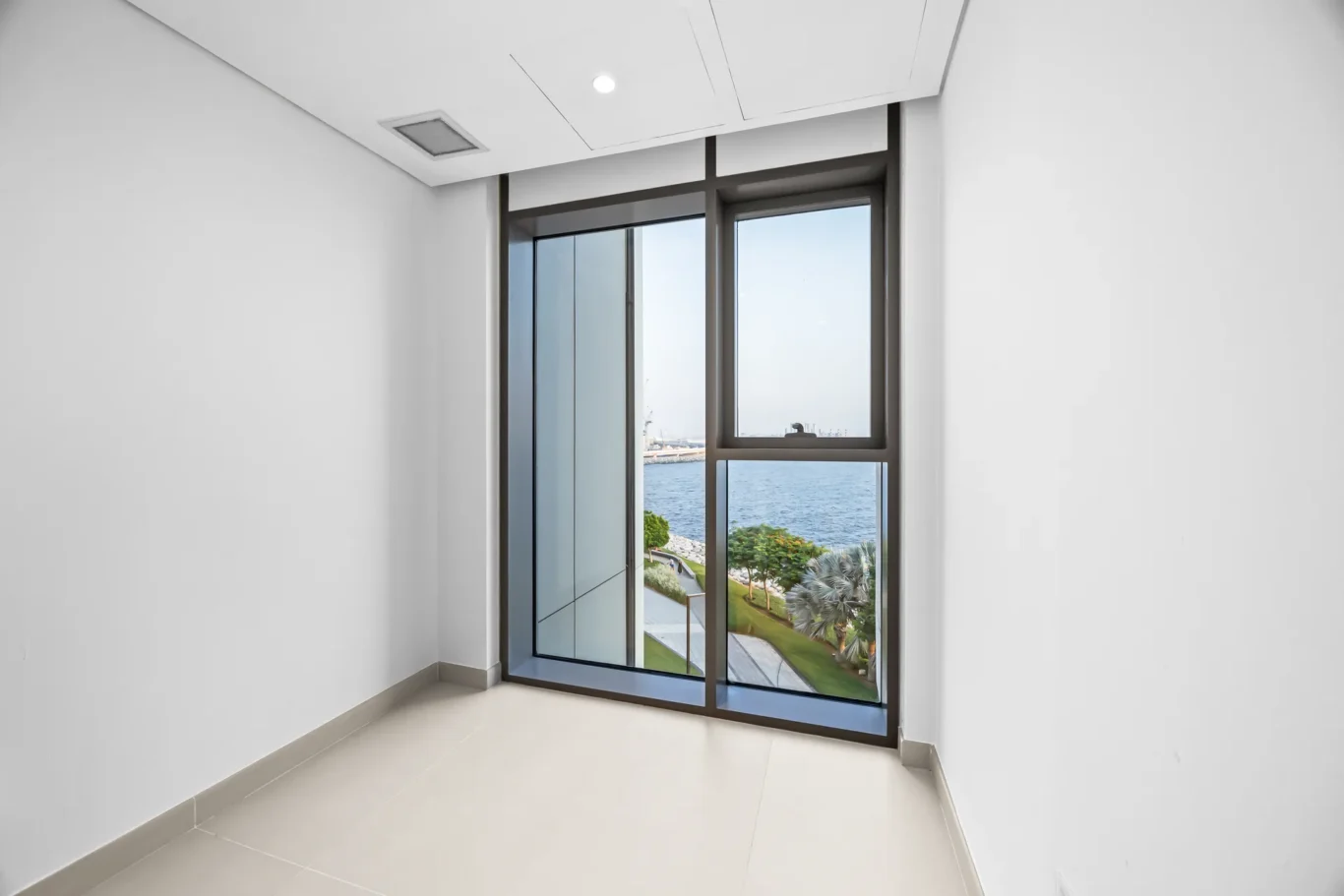 Bright narrow room with a large glass sliding door showing a seaside view and palm trees outside