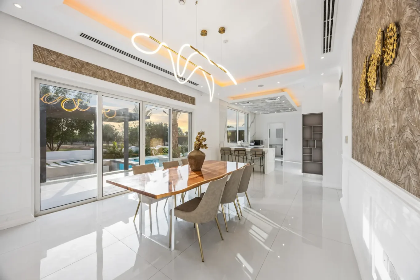 Bright open dining area with a wooden marble table and beige chairs, adjacent to sliding glass doors to an outdoor pool area