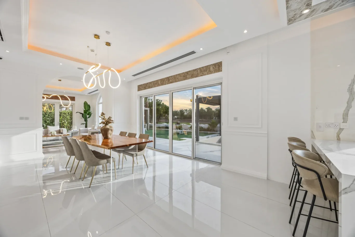 Bright modern dining area with a wooden table, gray chairs, marble island, and large sliding glass doors to the outdoors courtyard.