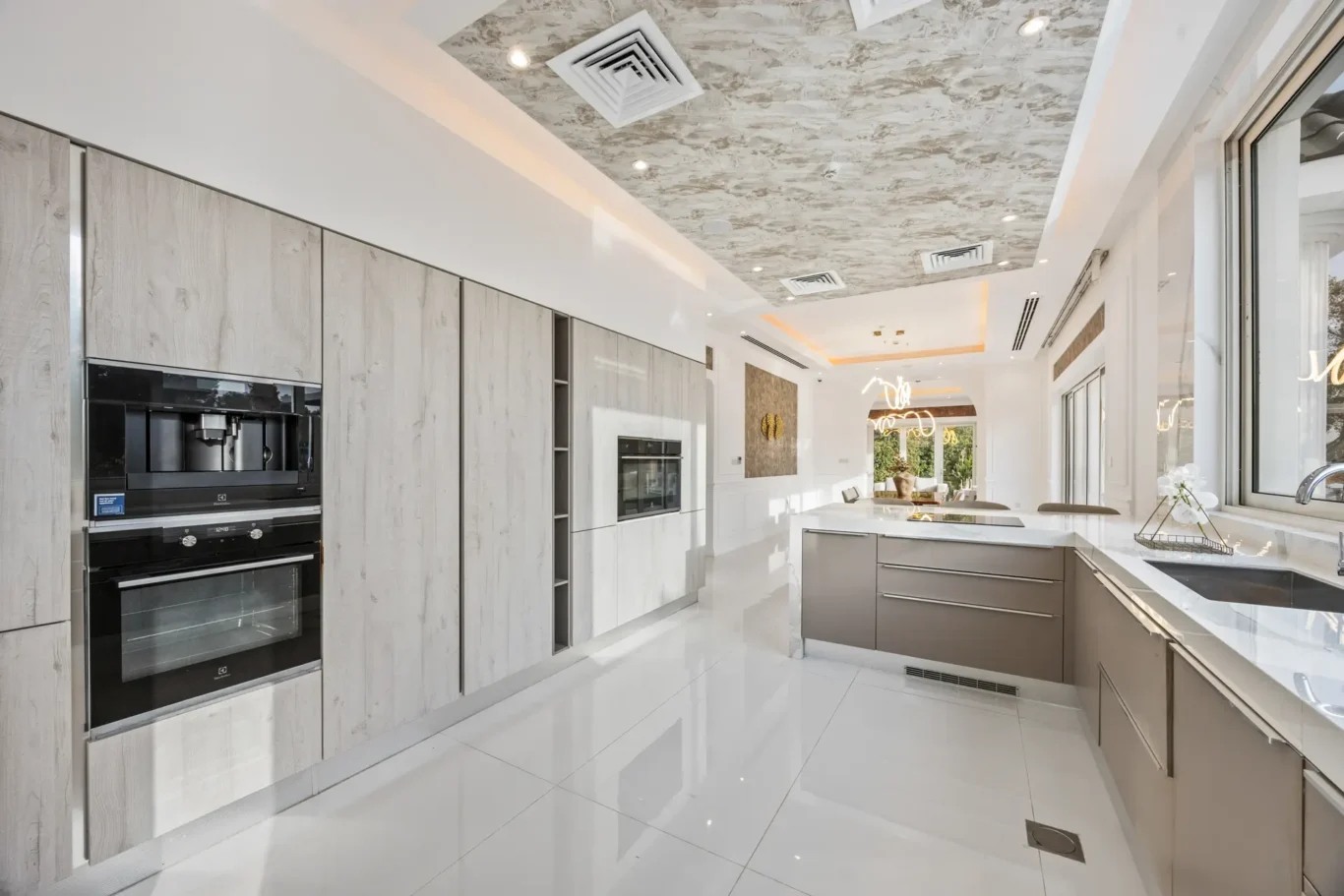 Modern kitchen with tall light-gray wood cabinets, built-in double ovens, a white glossy floor, and a central island. (Informative)