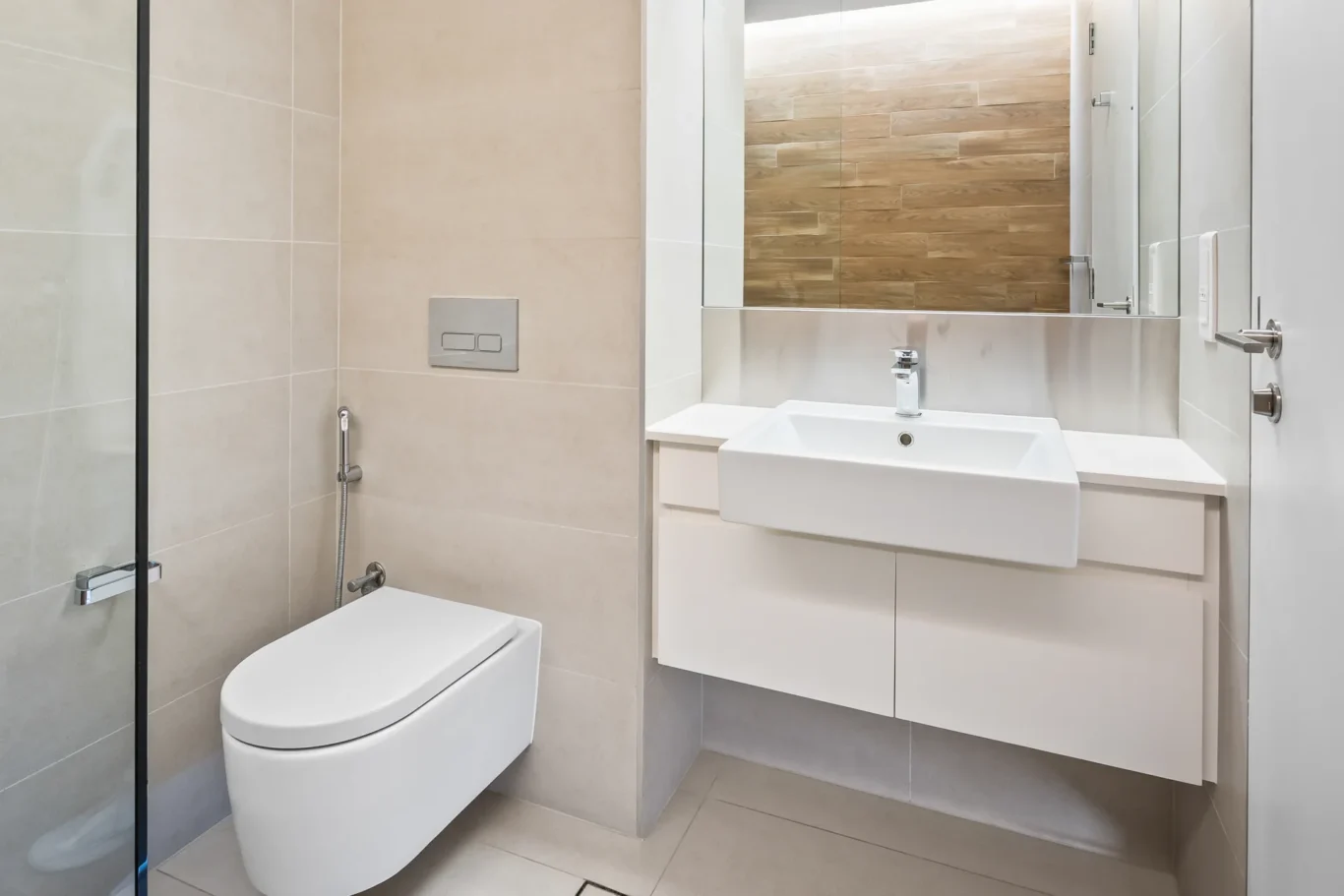 Modern bathroom with wall-mounted toilet, white sink, and large mirror above a minimal vanity.