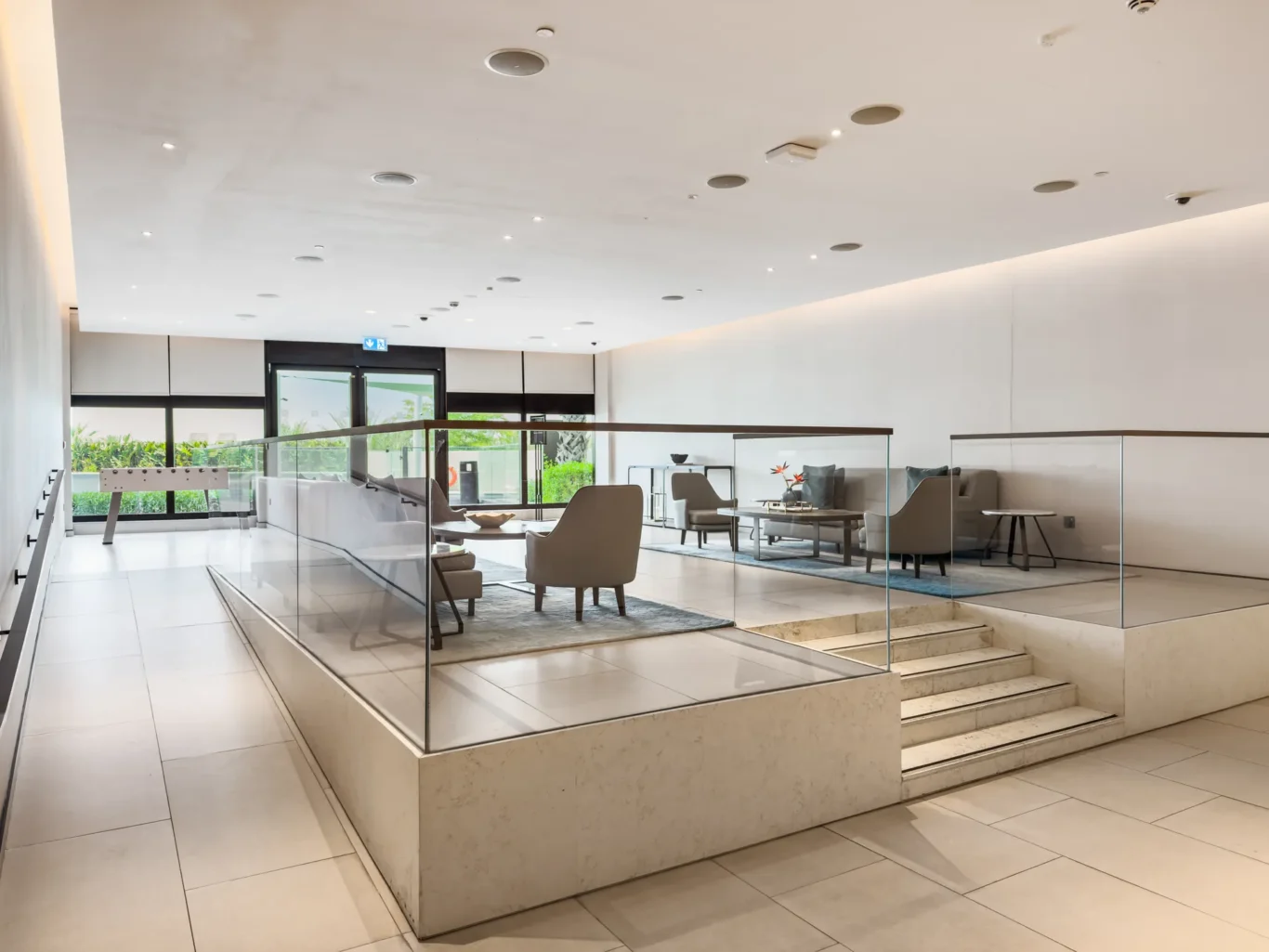Bright contemporary lobby with glass railings, marble steps, and seating areas by large windows.