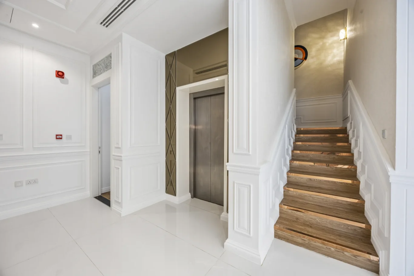 Elegant lobby area with elevator doors and a wooden staircase to the right.