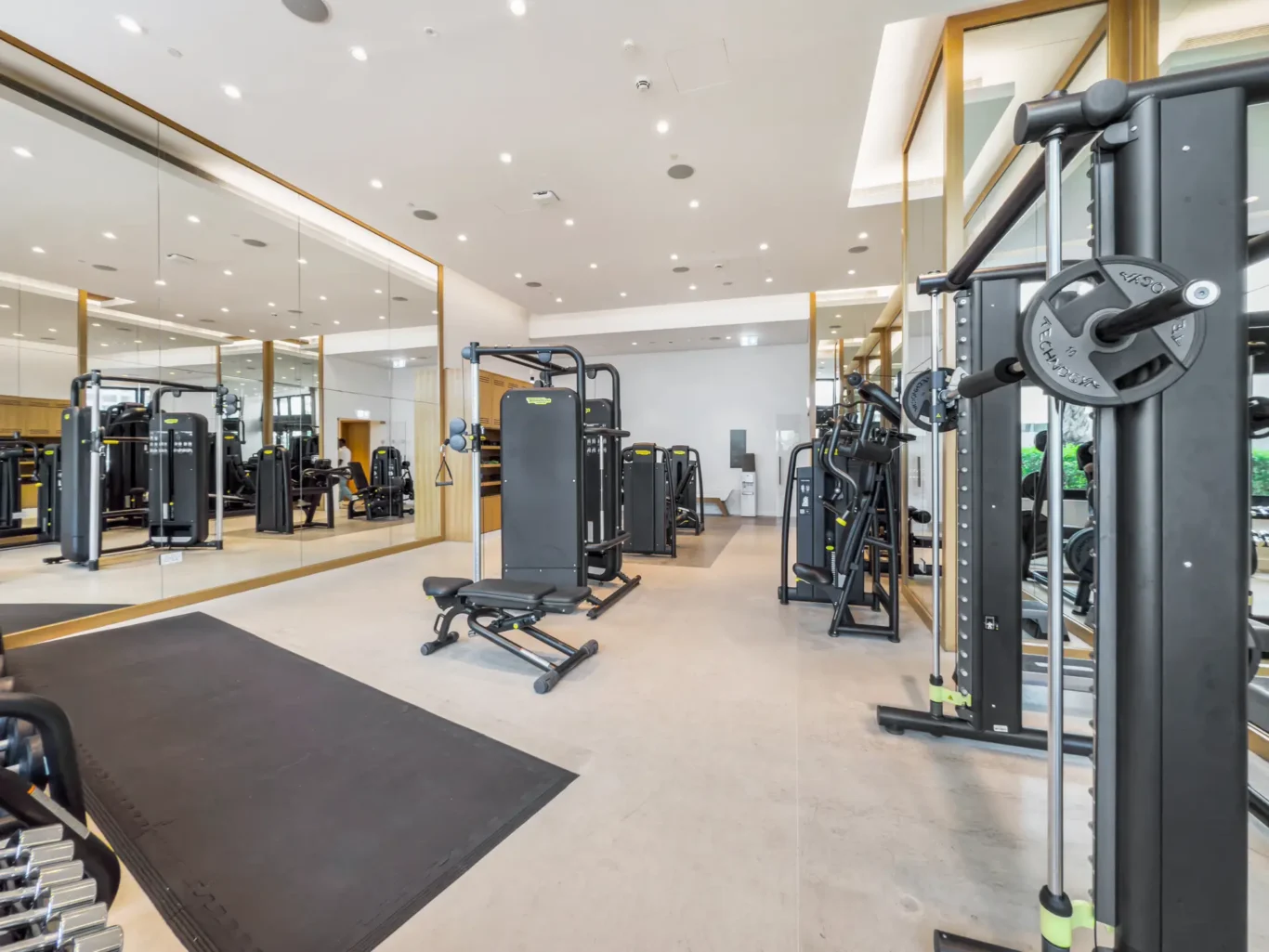 Well-lit fitness center featuring multi-station weight machines and free weights near mirrored walls.