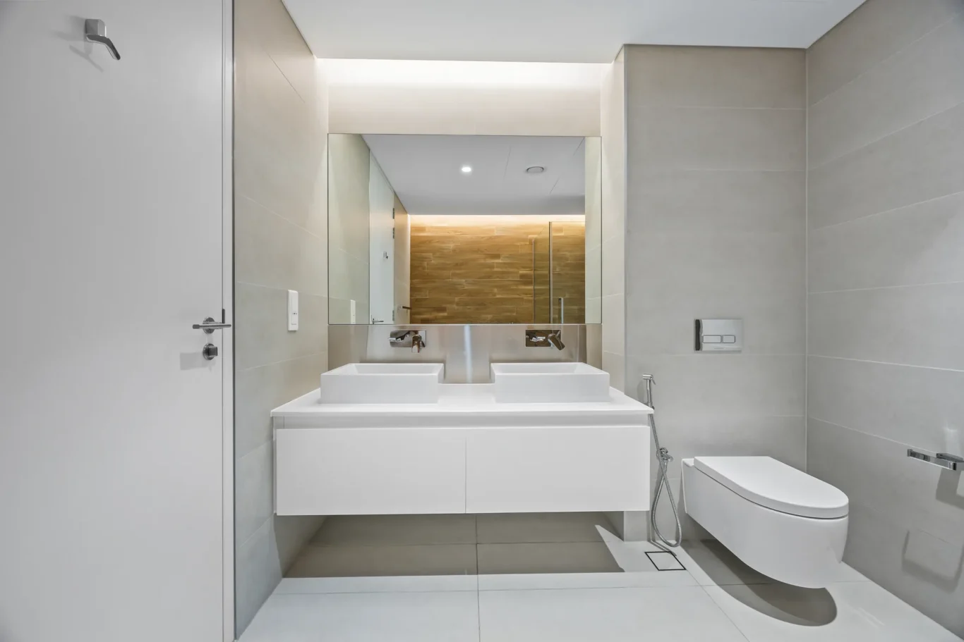 Modern bathroom with a floating double sink vanity, large wall mirror, and a wall-mounted toilet; wood-tiled shower area in back.