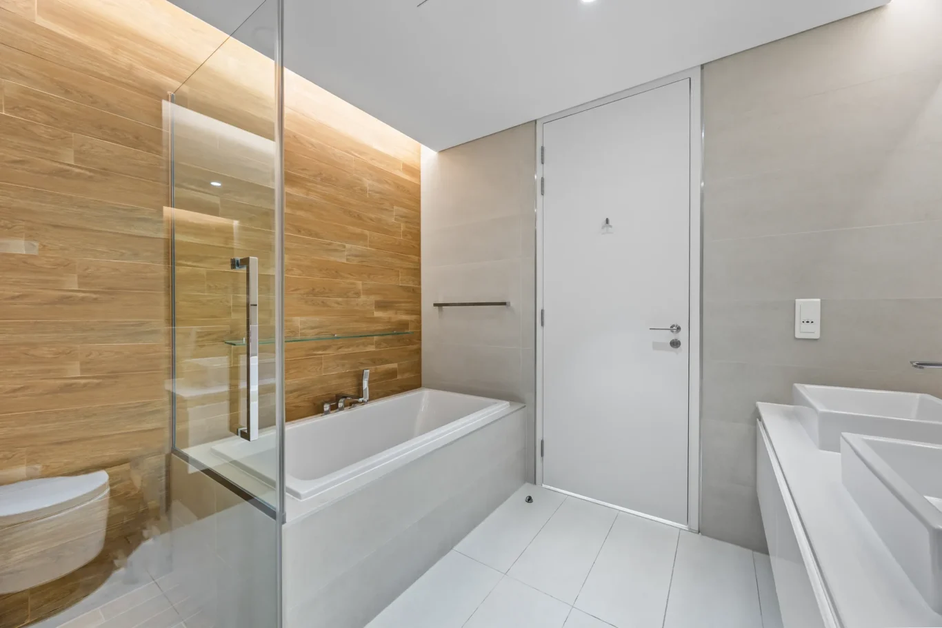 Modern bathroom with glass-enclosed shower, white tub, and wood-toned wall tiles.