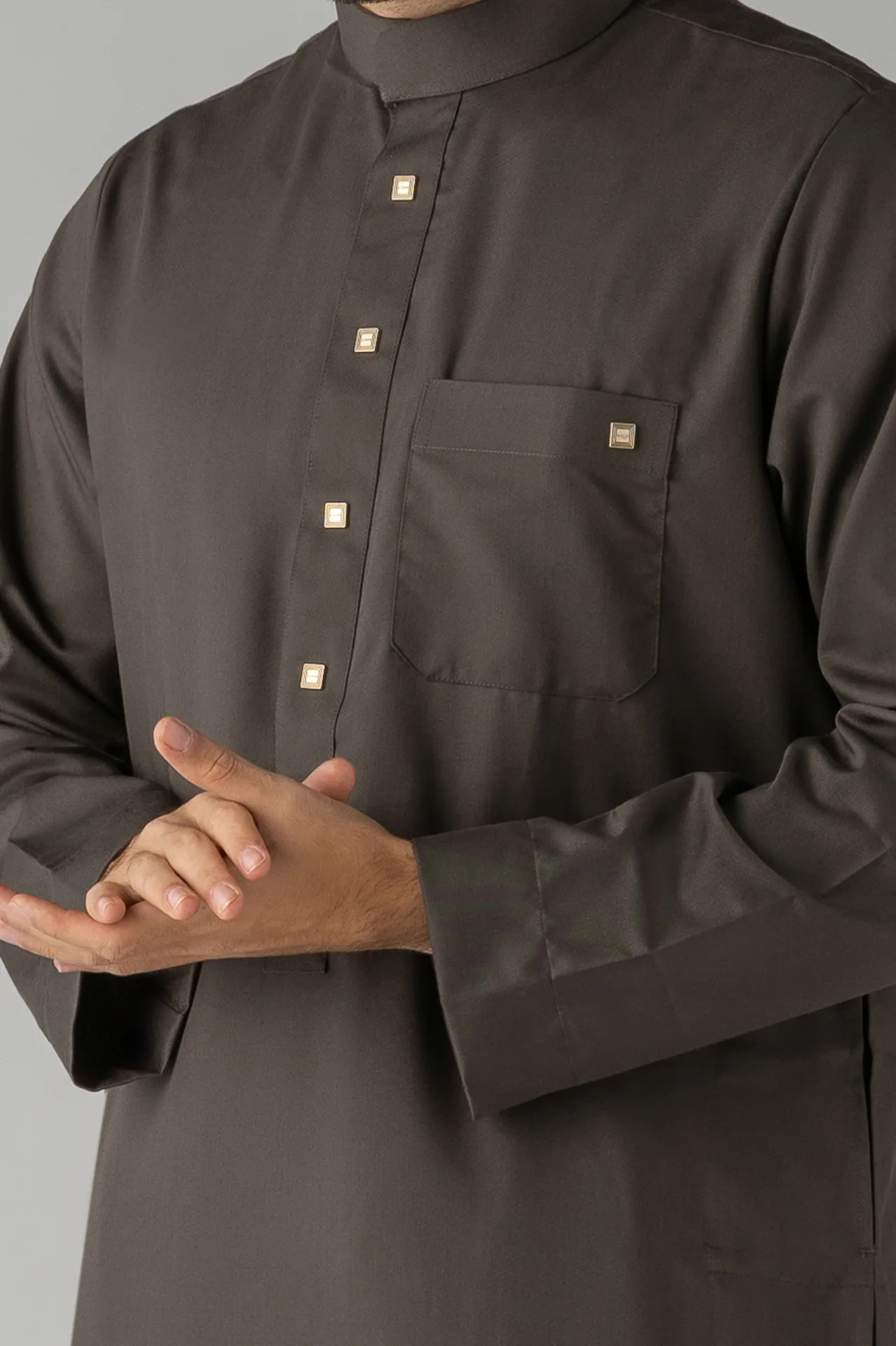 Man wearing a dark thobe with a pocket on the chest and small gold square buttons along the placket.