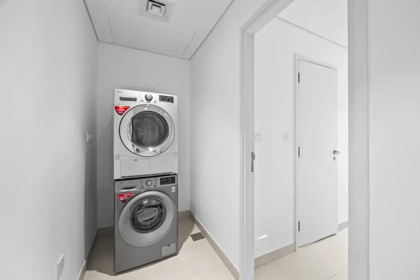 Stacked front-loading washer and dryer in a narrow laundry closet beside a white door.