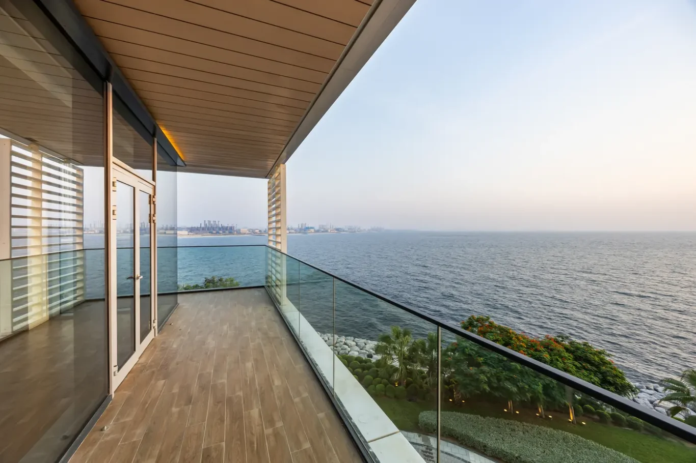 Modern balcony with glass railing and sliding doors, overlooking the sea at sunset. (informative)