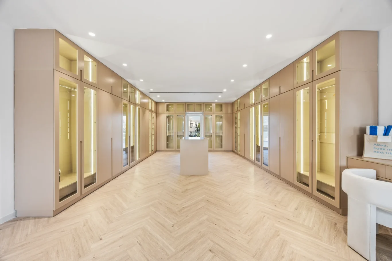 Showroom corridor with beige built-in cabinets and glass doors along both walls, bright overhead lighting and a central island.