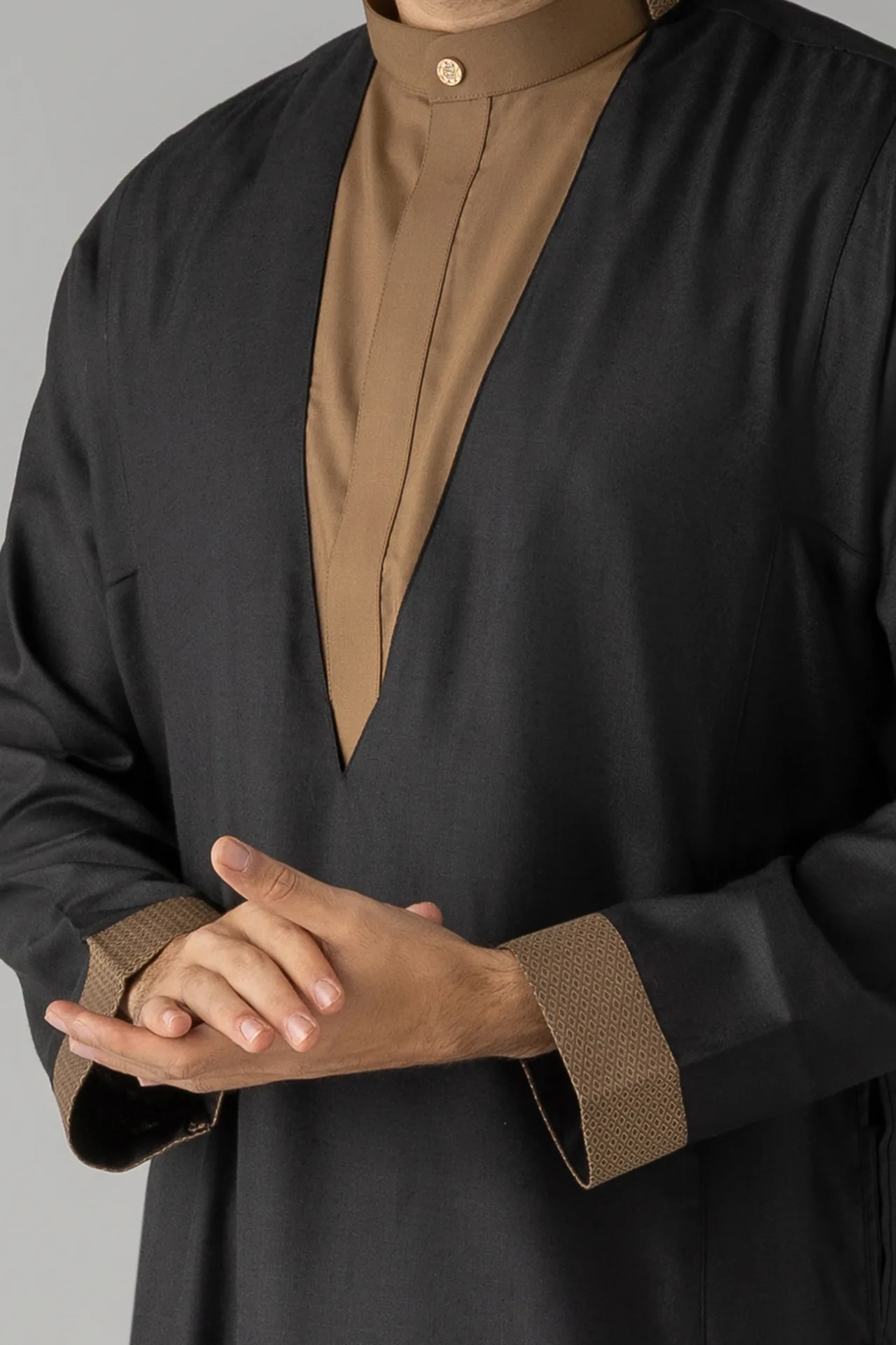 Person wearing a black robe with a tan-brown inner panel and patterned cuffs, hands gently clasped in front.