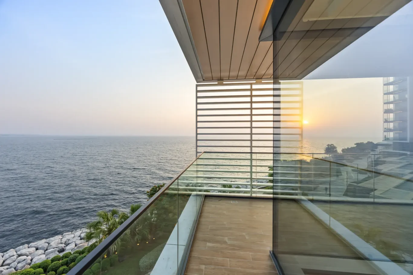 Modern glass balcony overlooking the ocean at sunset from a contemporary terrace.