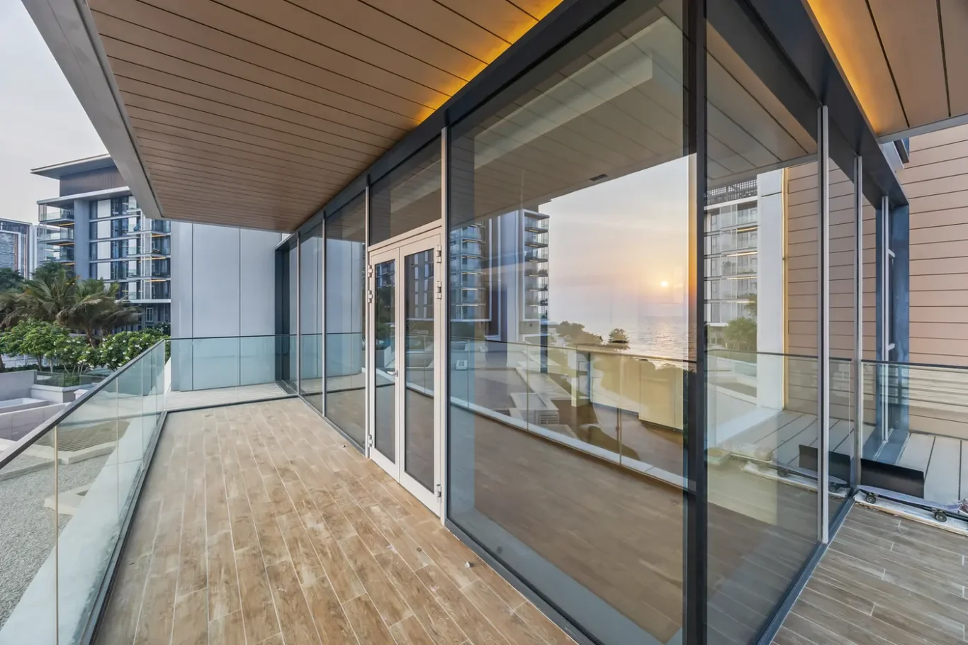 Modern balcony with glass railing and floor-to-ceiling windows overlooking the sea at sunset.