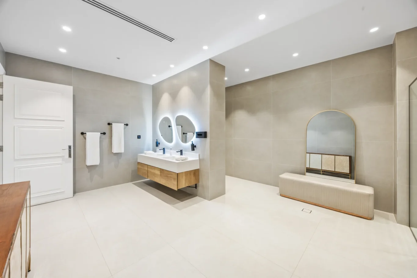 Modern bathroom with a double vanity, round backlit mirrors, and a cushioned bench.