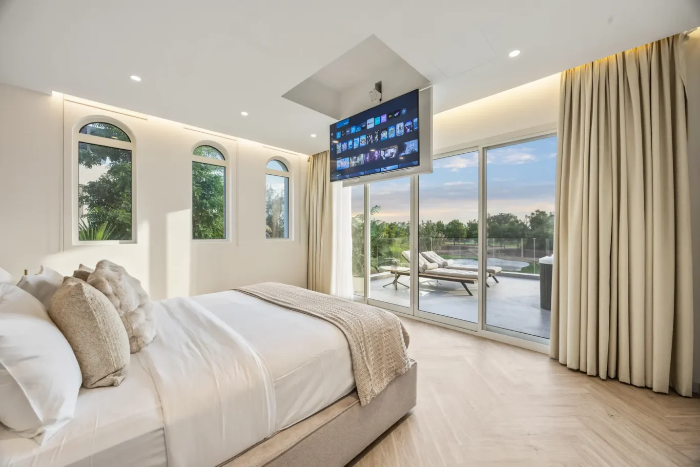 Bright bedroom with a wall-mounted TV above the bed and large sliding glass doors to a patio.