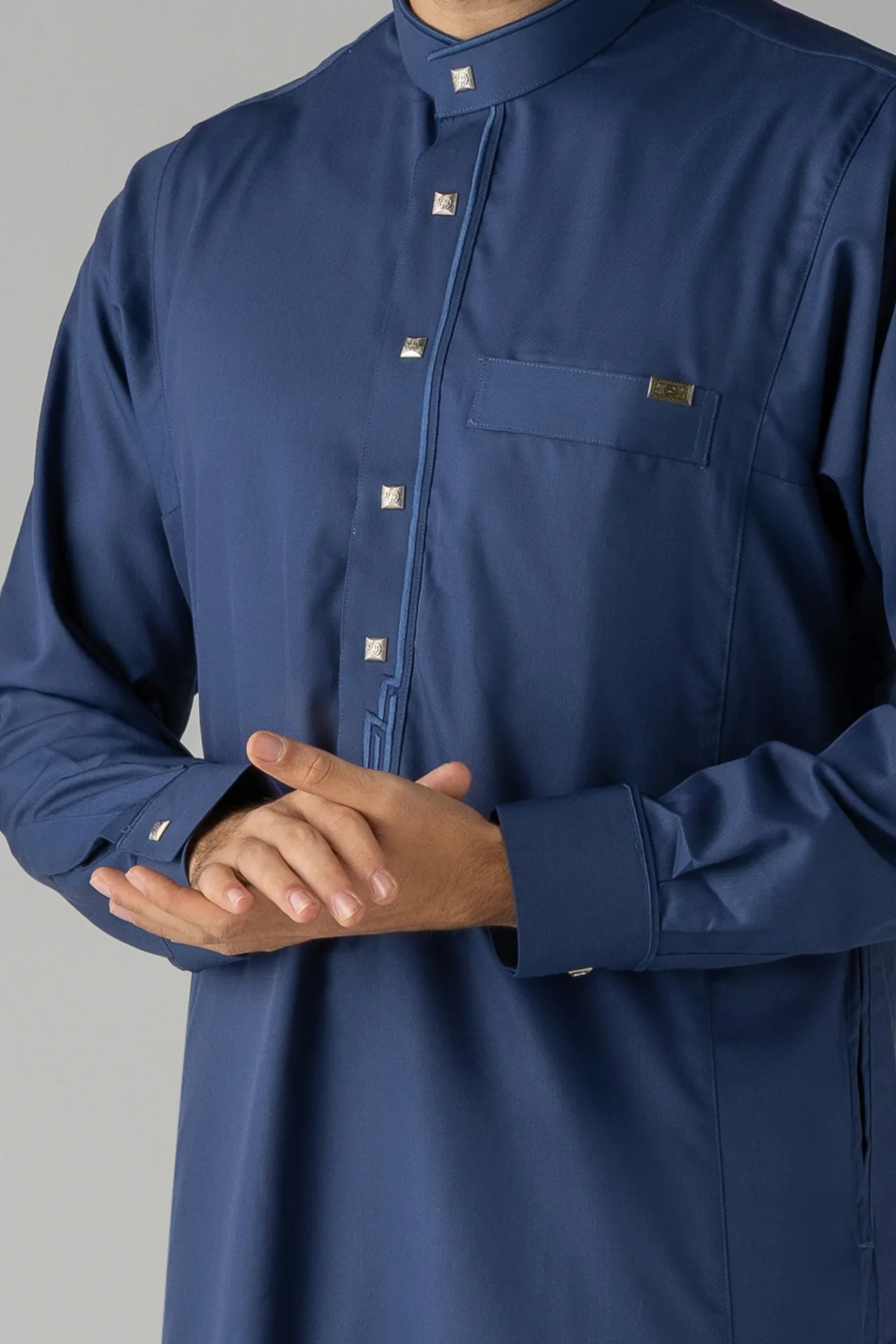 Close-up of a navy traditional thobe with square metal studs along the placket and a chest pocket.