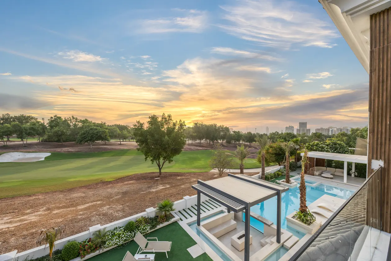 Modern backyard with a rectangular pool, lounge chairs, and a pergola, overlooking a green golf course at sunset.