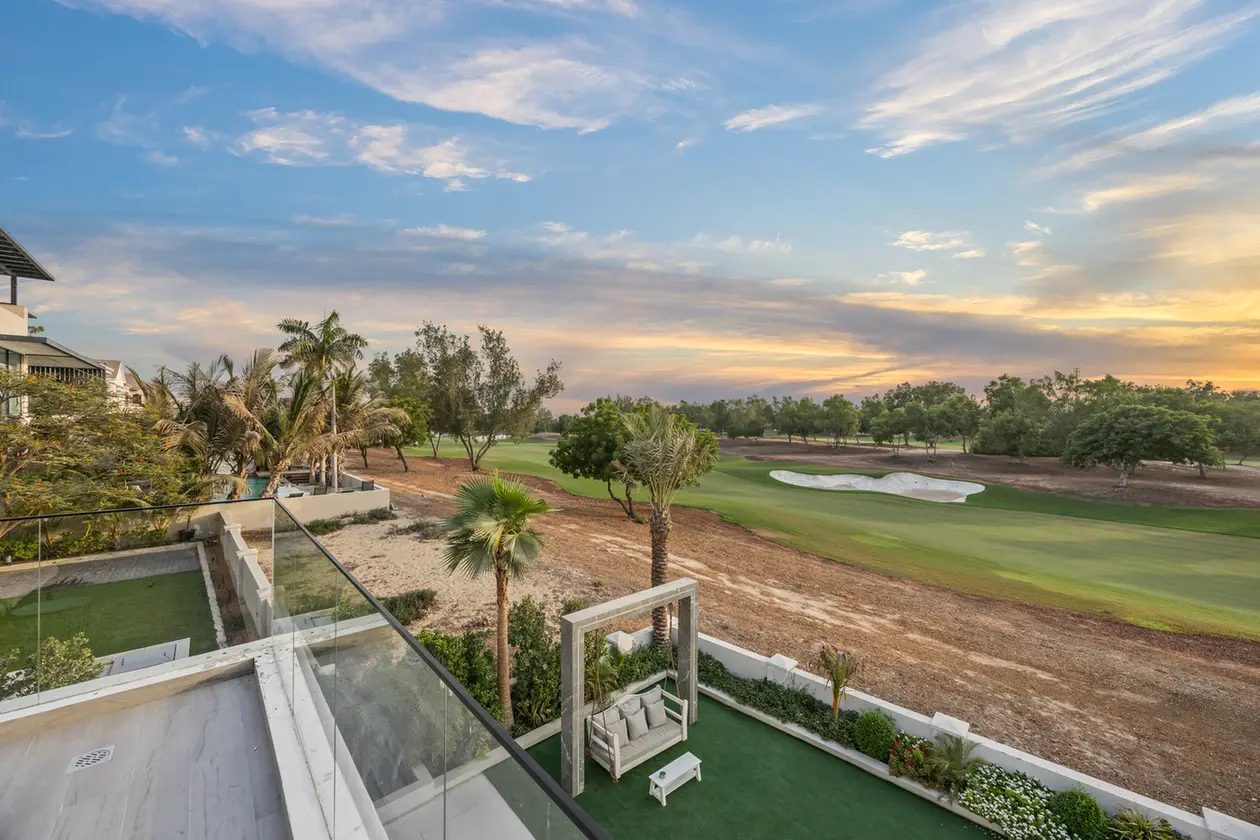Balcony seating area overlooking a golf course with trees and a sand bunker at sunset