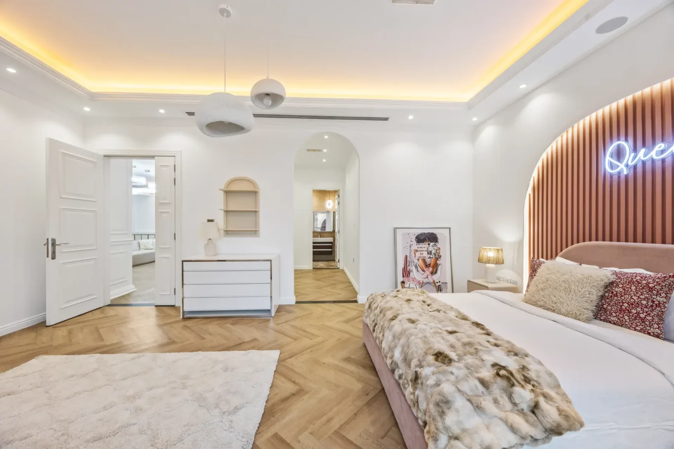 Bright modern bedroom with two beds, fur throws, and a neon 'Queen' sign on a curved wooden wall paneling.