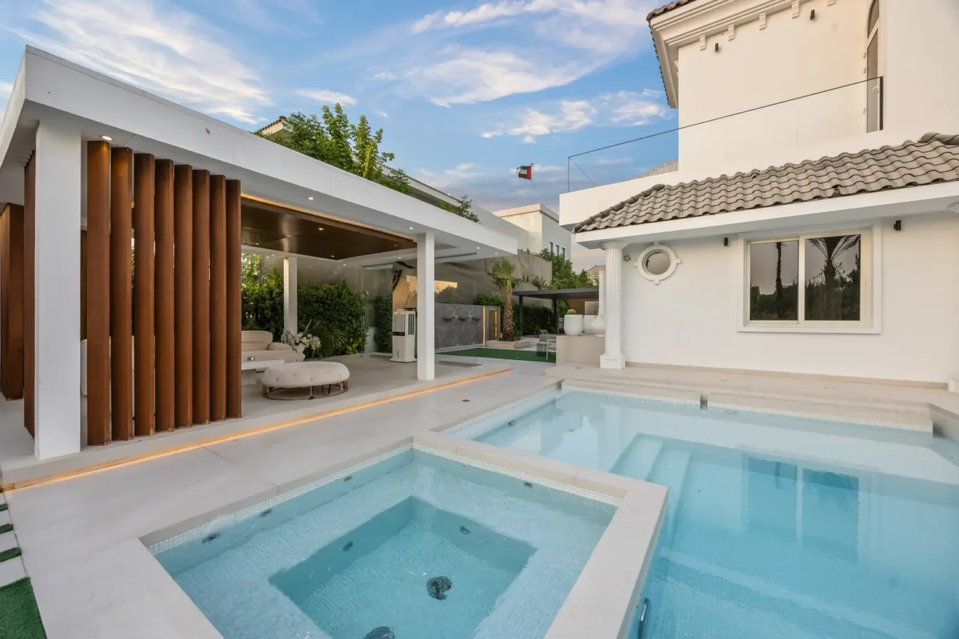 Modern white villa with a blue pool, outdoor seating under a covered lounge area and vertical wooden slats on the left.