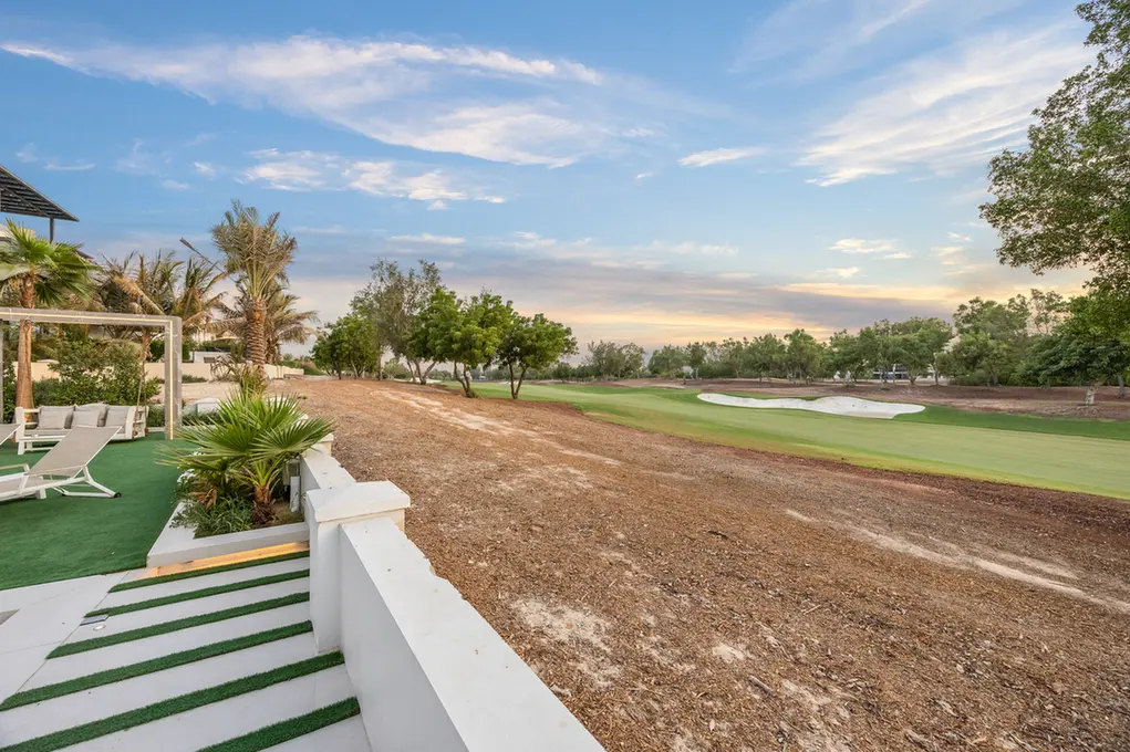 Terraced patio with loungers overlooking a golf course fairway and sand bunker at sunset or dusk light.