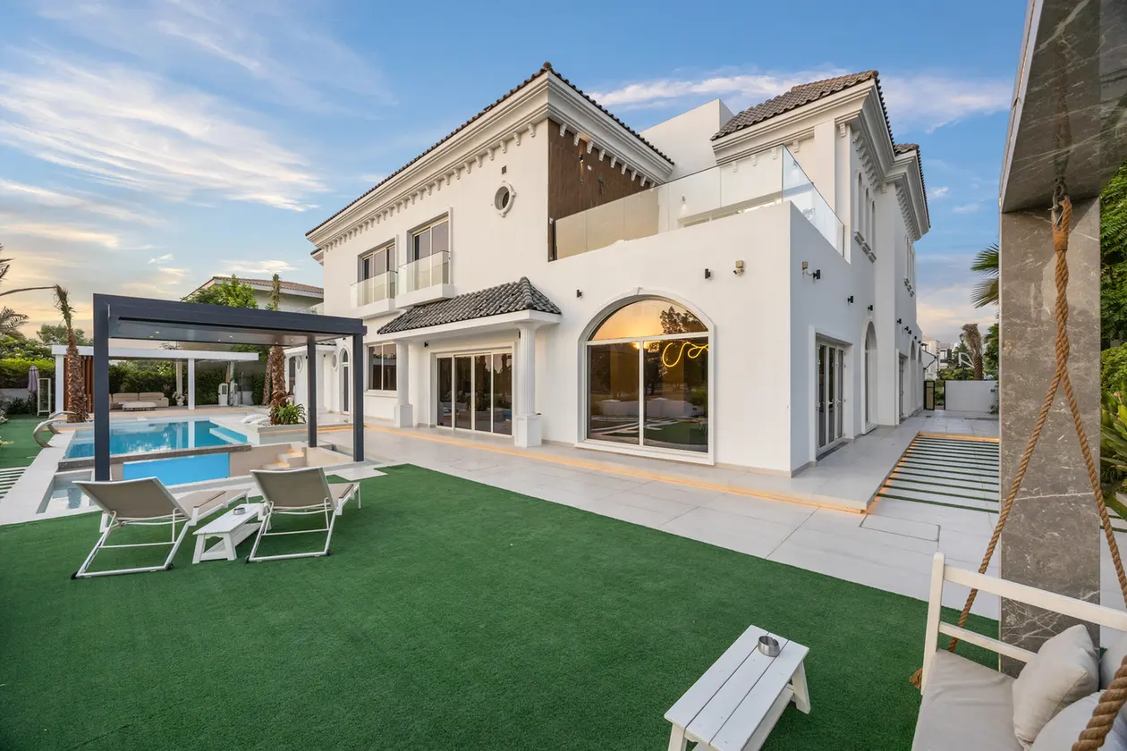 Modern white villa with a pool and lawned backyard, lounge chairs, and a shaded seating area. Thermally-lit interior rooms visible through large glass doors.