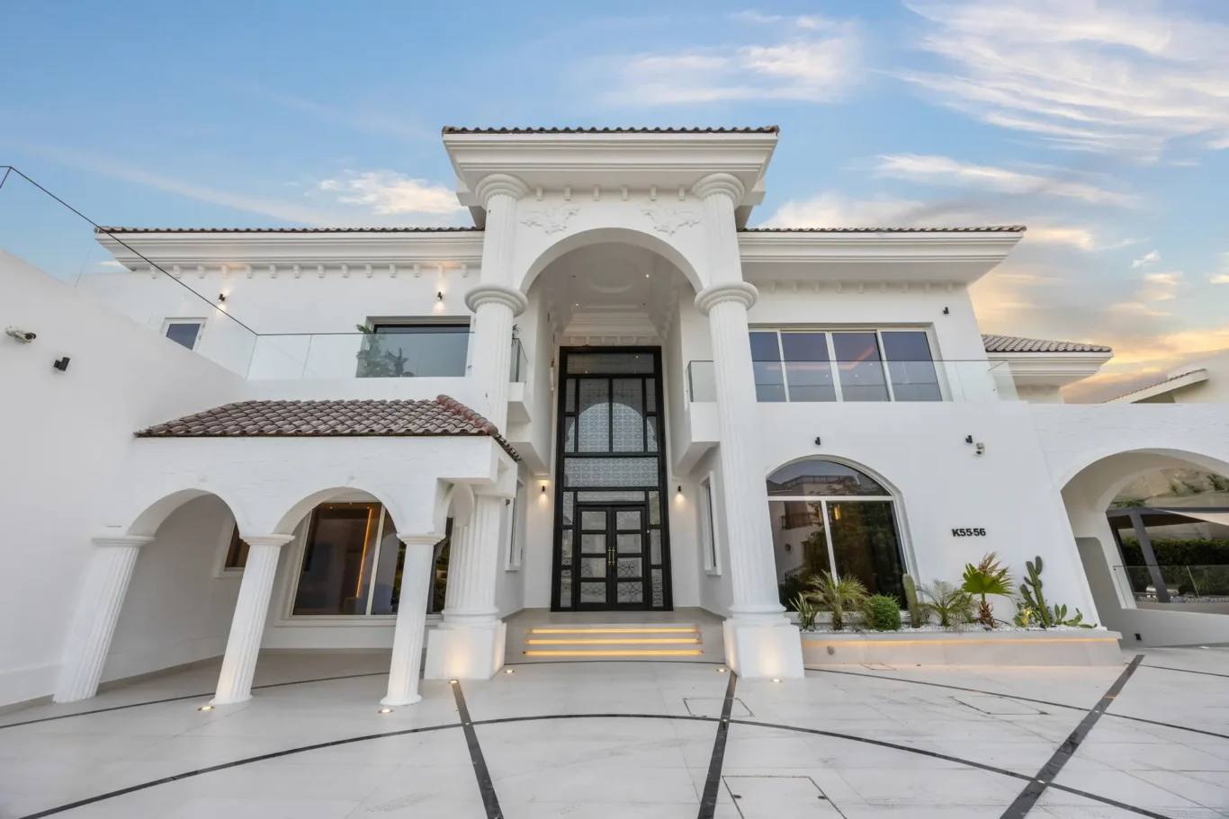 White luxury mansion with a columned entrance, arched doorway, and blue sky above.