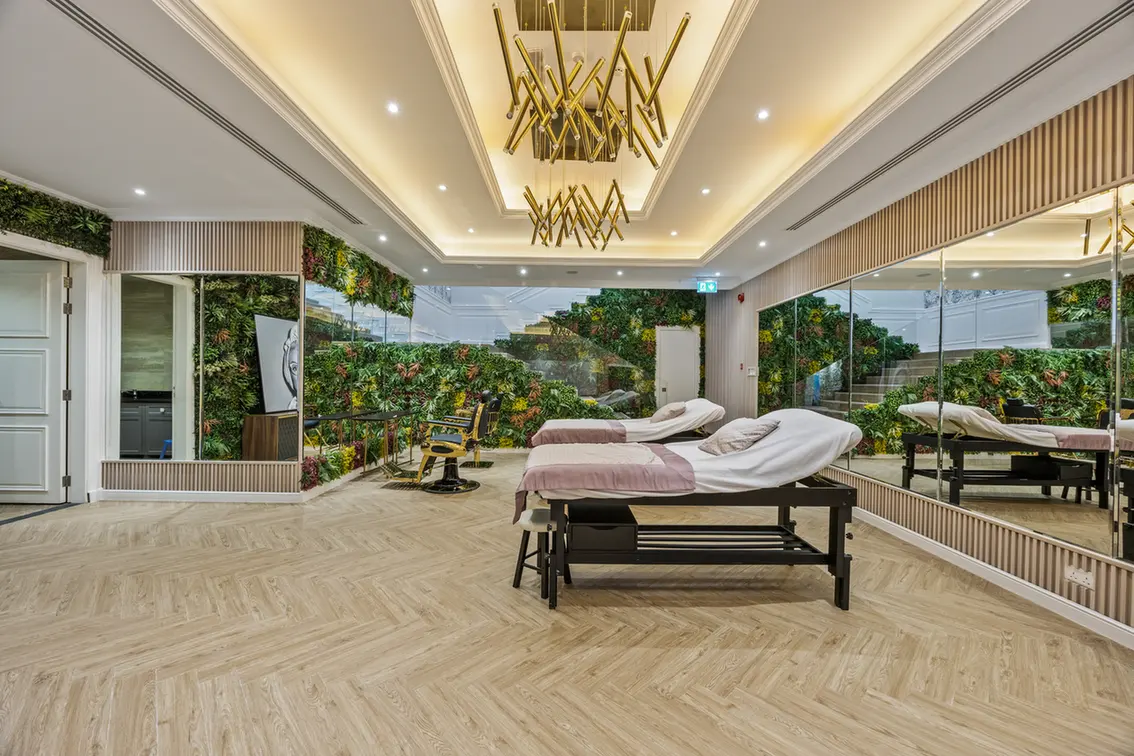 Spa treatment room with two massage tables, mirrored walls, and a lush green vertical garden.