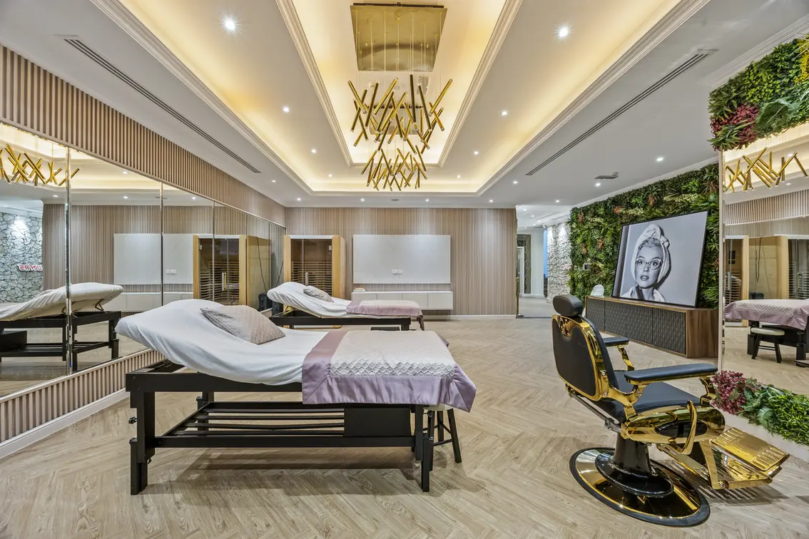 Luxurious spa treatment room with two massage beds, pastel linens, wood floors, and mirrored walls with gold accents.