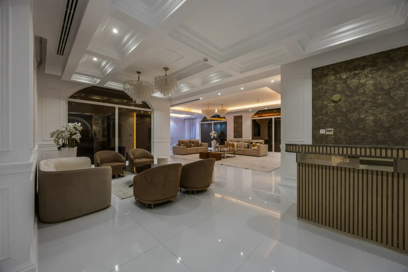 Luxurious showroom-style living room with beige curved sofas, glass coffee tables, and crystal chandeliers in a bright white space.