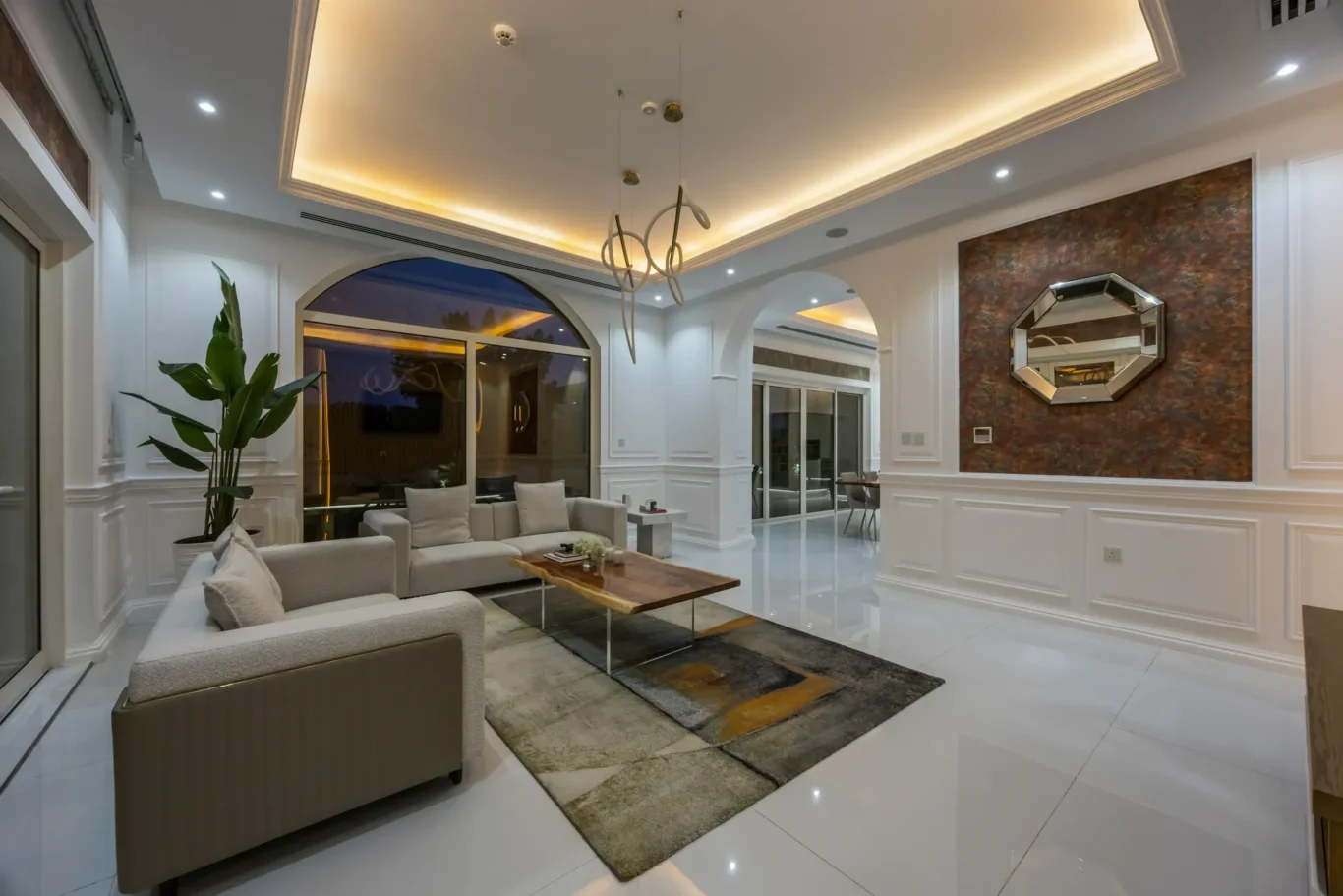 Luxurious white living room with beige sofas, a wooden coffee table, and a green potted plant under soft ceiling lighting at dusk