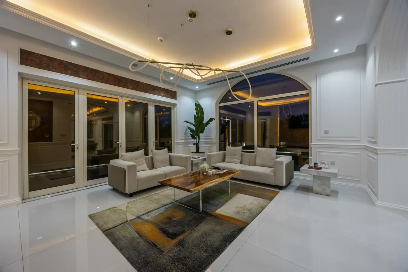 Bright modern living room with white paneled walls, arched window, glass doors, beige sectional sofa, and a wood coffee table. 王