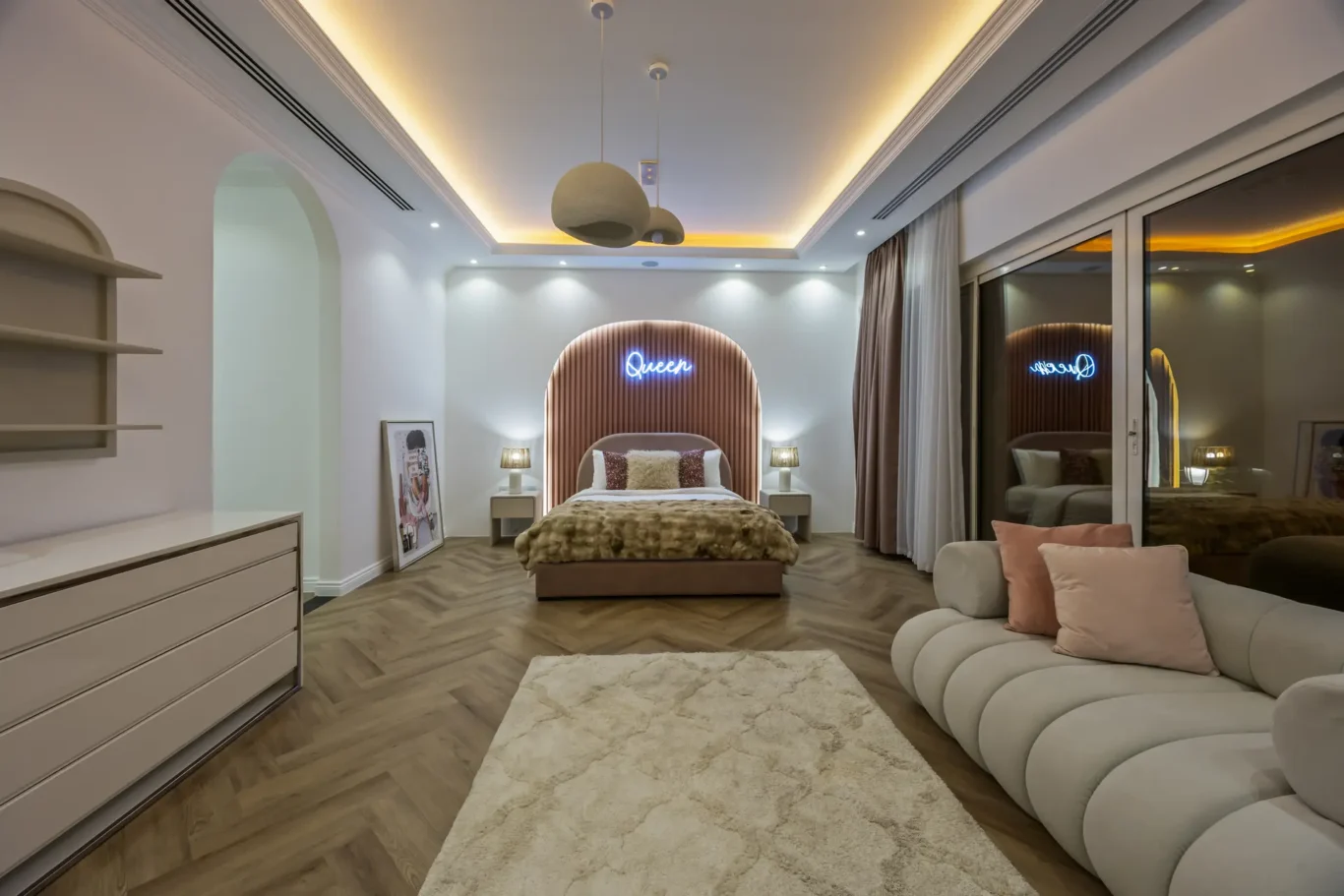 Luxurious bedroom with a padded arc headboard, fur bedding, and a neon 'Queen' sign above the bed.