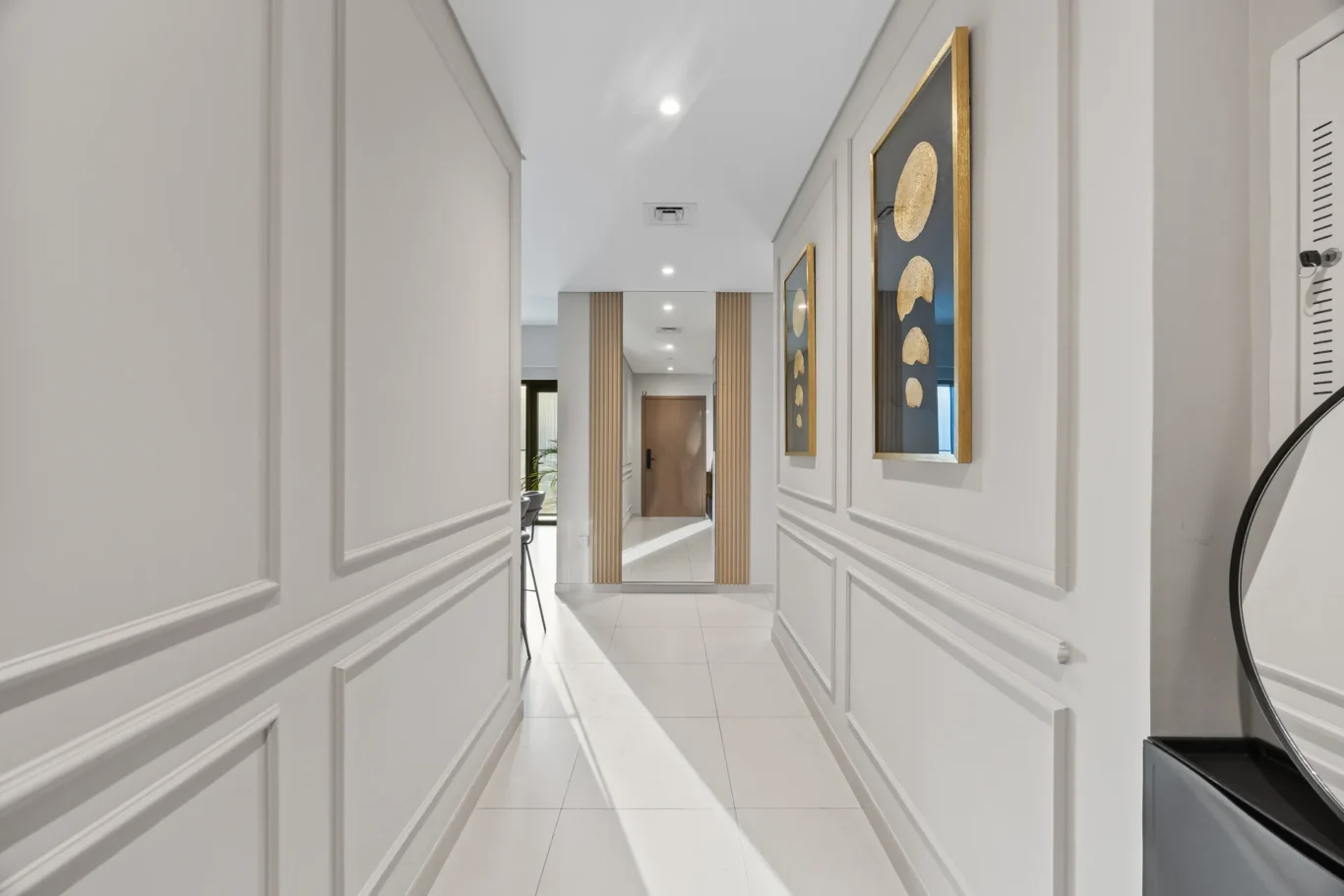 Bright, modern hallway with white paneled walls and gold-framed mirrors at the right end of the corridor