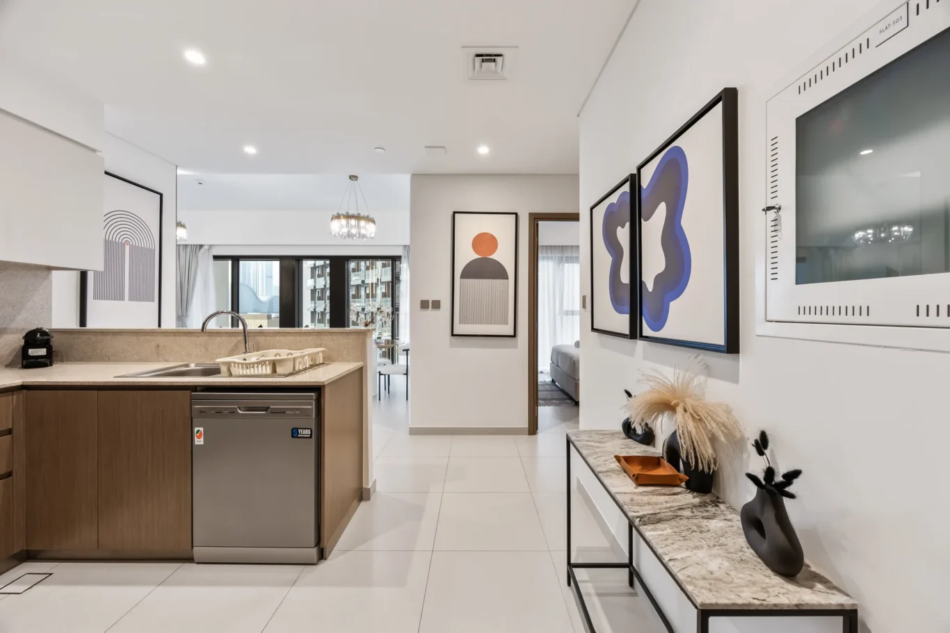 Open-plan kitchen with an island, sink, and a built-in dishwasher, plus framed abstract art on the walls.