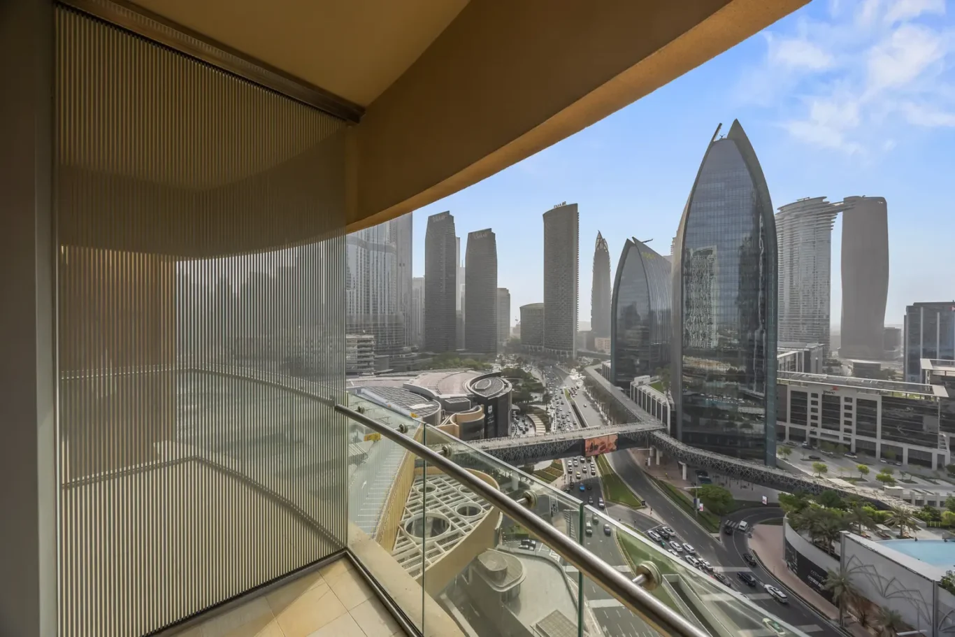 Balcony view of Dubai's modern skyline with glass skyscrapers, elevated roads, and a curved pedestrian bridge.