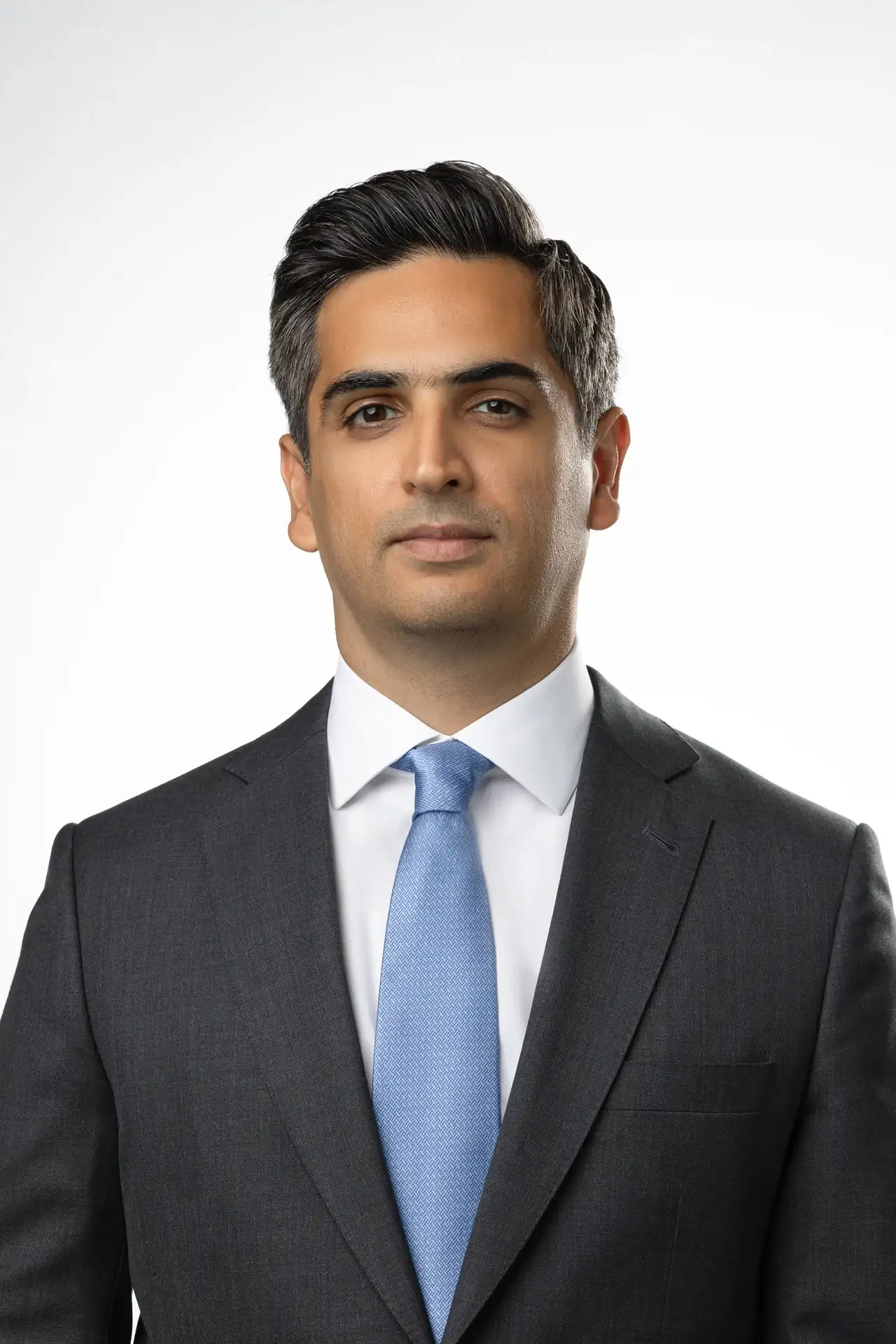 Professional headshot of a man in a dark suit and light blue tie, facing the camera against a neutral background.