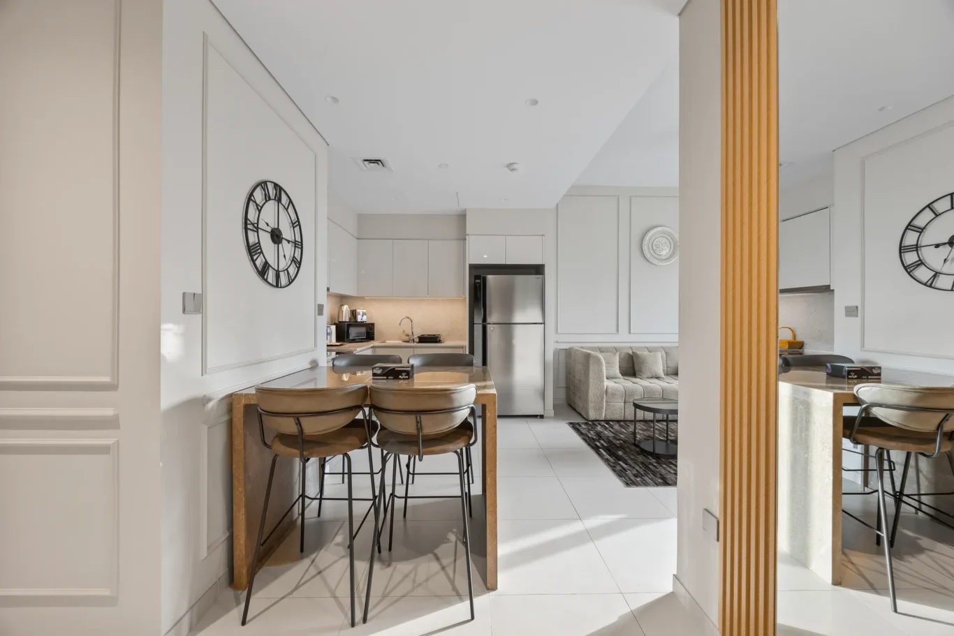 Open-concept kitchen and living area with white cabinets, stainless fridge, and a wooden dining table with metal stools.