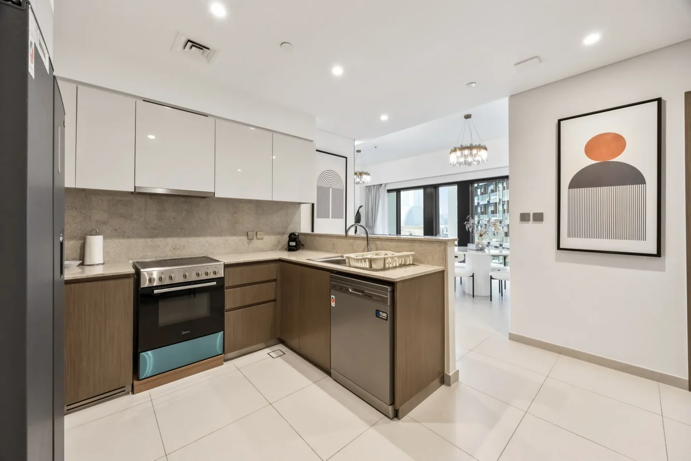 Modern open-plan kitchen with white upper cabinets, wooden lower cabinetry, stainless-steel appliances, and an abstract framed wall art in the dining area