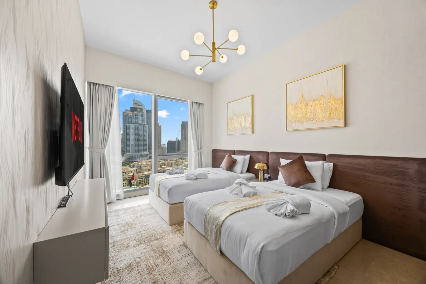 Hotel room with two twin beds, plush headboards, and a city skyline view through large windows.