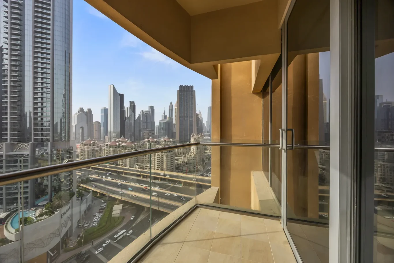 Balcony with glass railing overlooks a dense cityscape of modern high-rise buildings under a clear blue sky.
