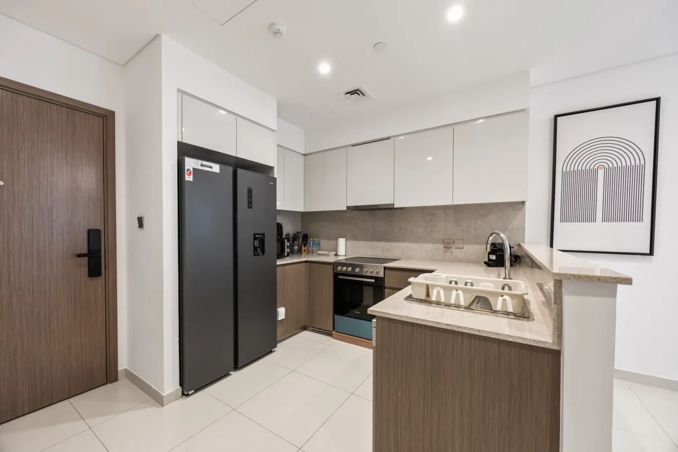 Modern kitchen with white upper cabinets, wood lower cabinets, a dark fridge, and a large framed abstract print on the wall.