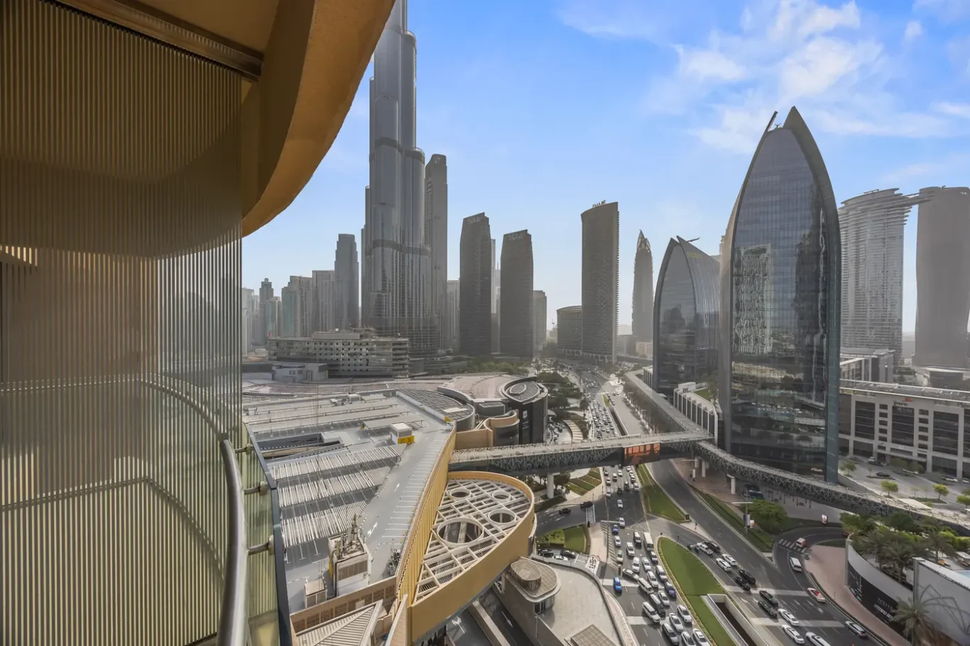 Wide cityscape of a modern financial district with tall glass skyscrapers, elevated highways, and a busy road network viewed from a glass-walled terrace on the left.