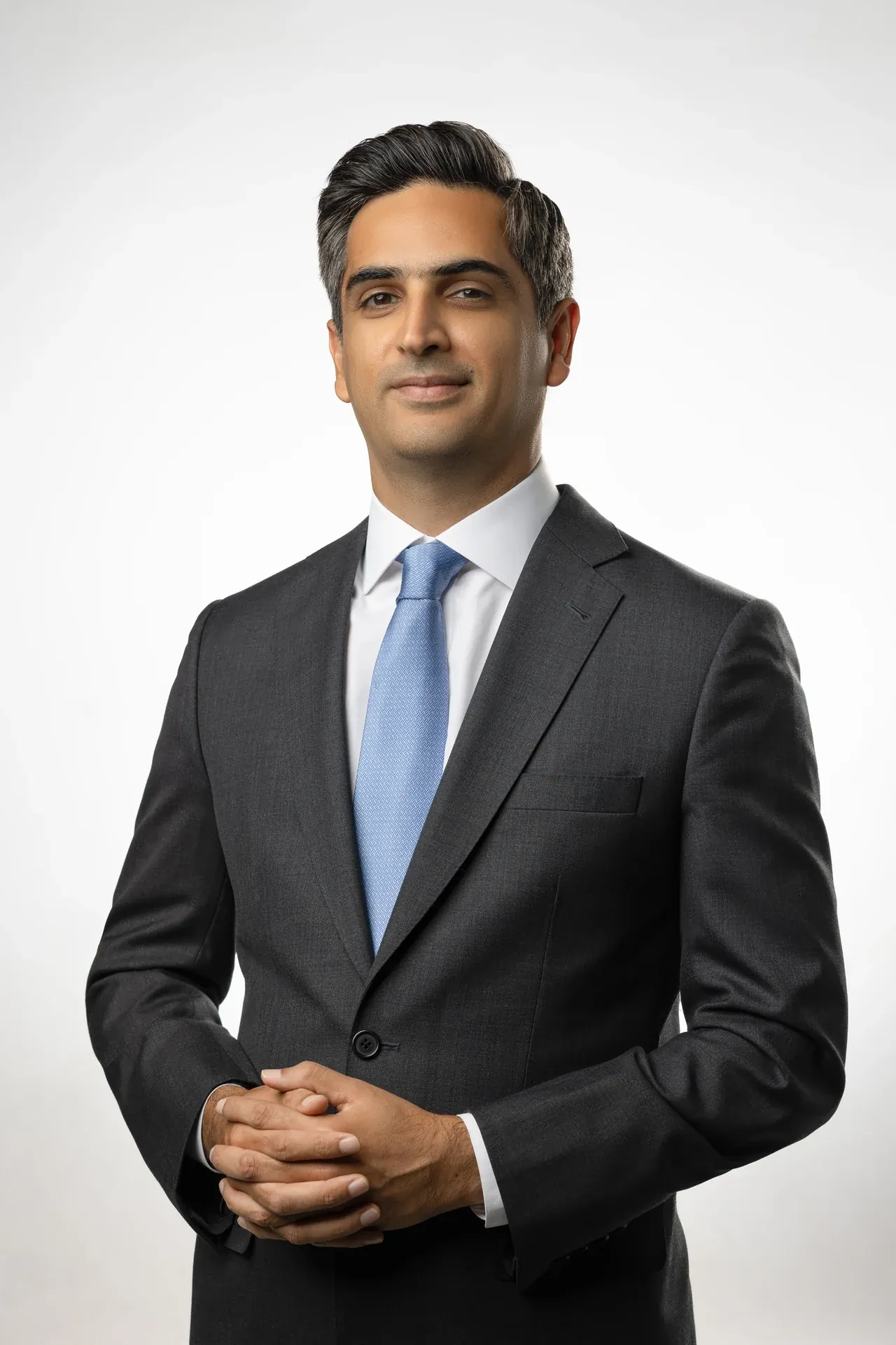 Professional portrait of a man in a dark suit and light blue tie, posed against a neutral background.