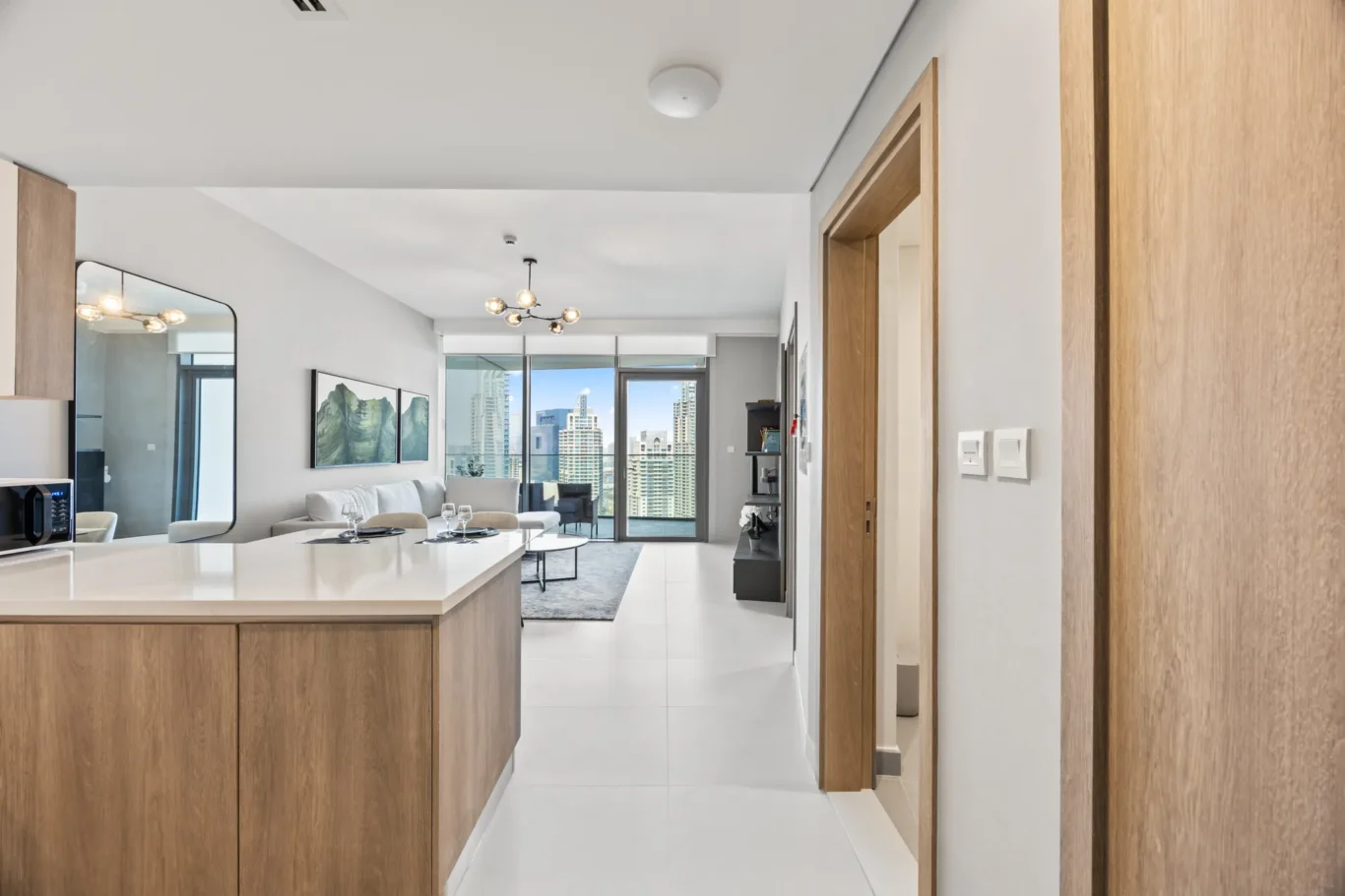 Open-plan modern kitchen and living area with a white island, wooden cabinets, and a city skyline view through large windows.