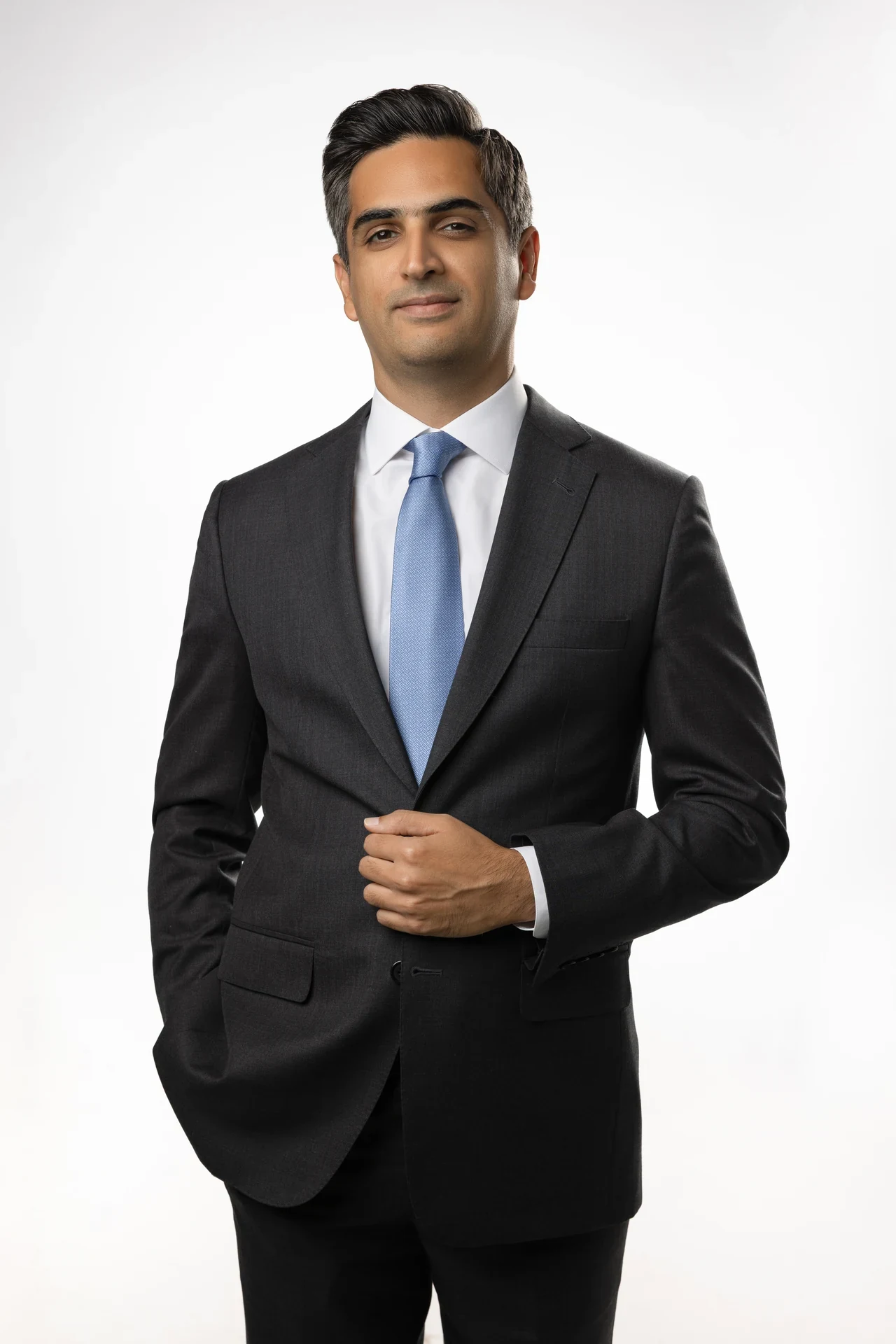 Professional man in a dark suit and blue tie, standing against a plain white background in a corporate headshot.